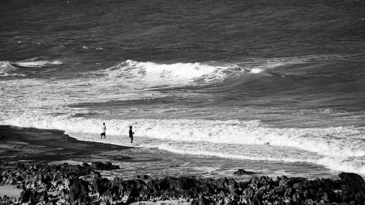 Black and white photo of two fishermen on the rocky shore in Natal, Brazil.